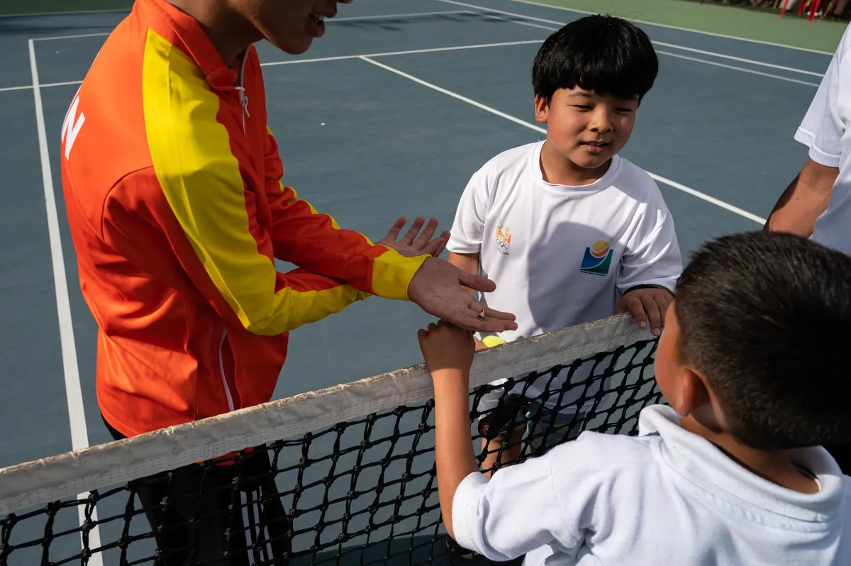 A BTF coach in the federation tracksuit talking a young player through a point at the net