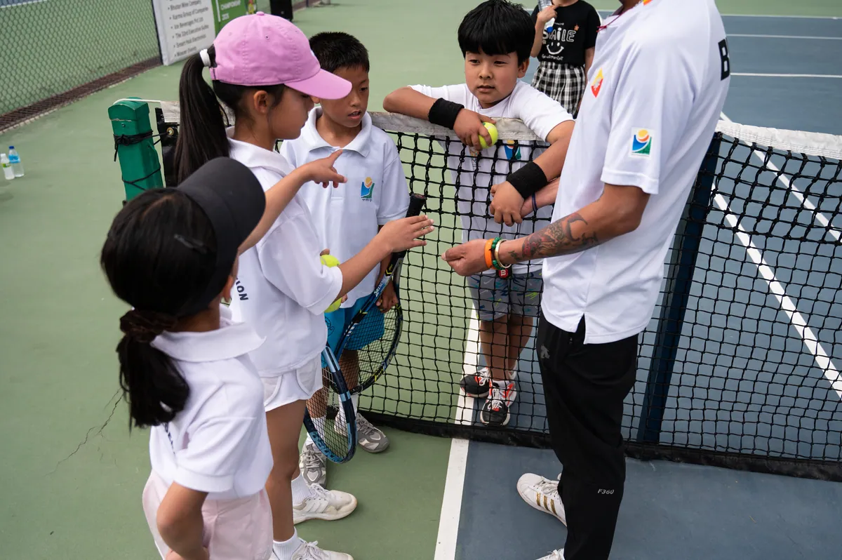 A coach surrounded by junior players at the net at the National Tennis Centre