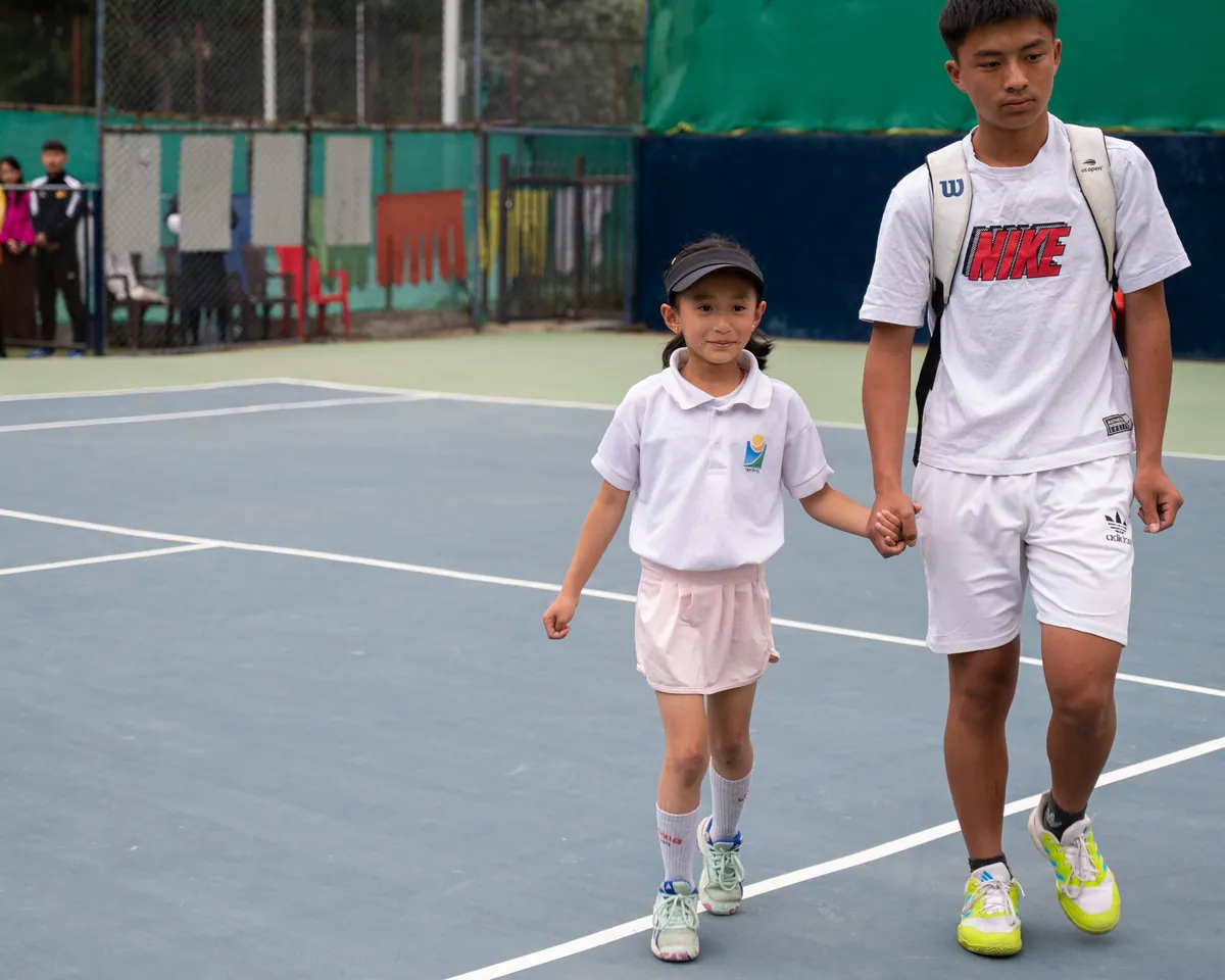 An older player walking a small girl onto court by the hand before her match