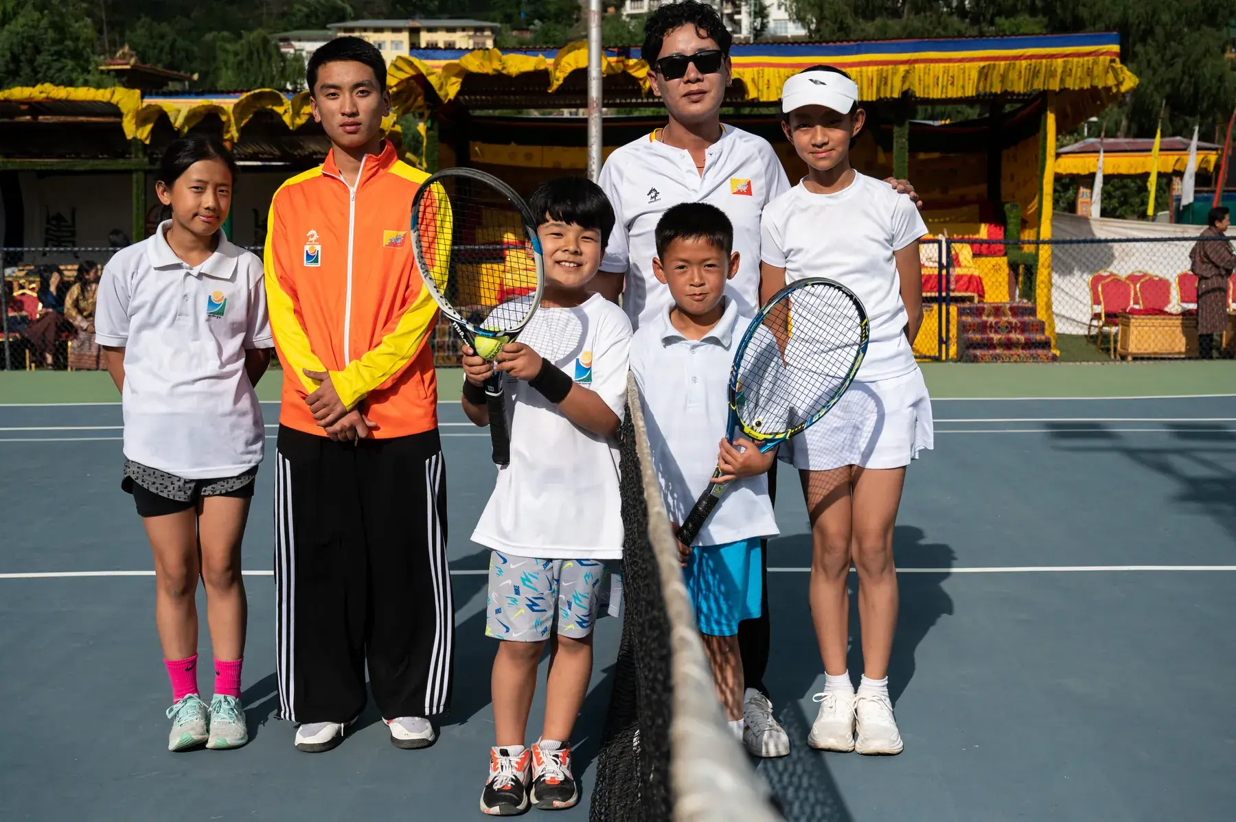 Coaches and junior players lined up across the net for a group photograph at a junior tournament