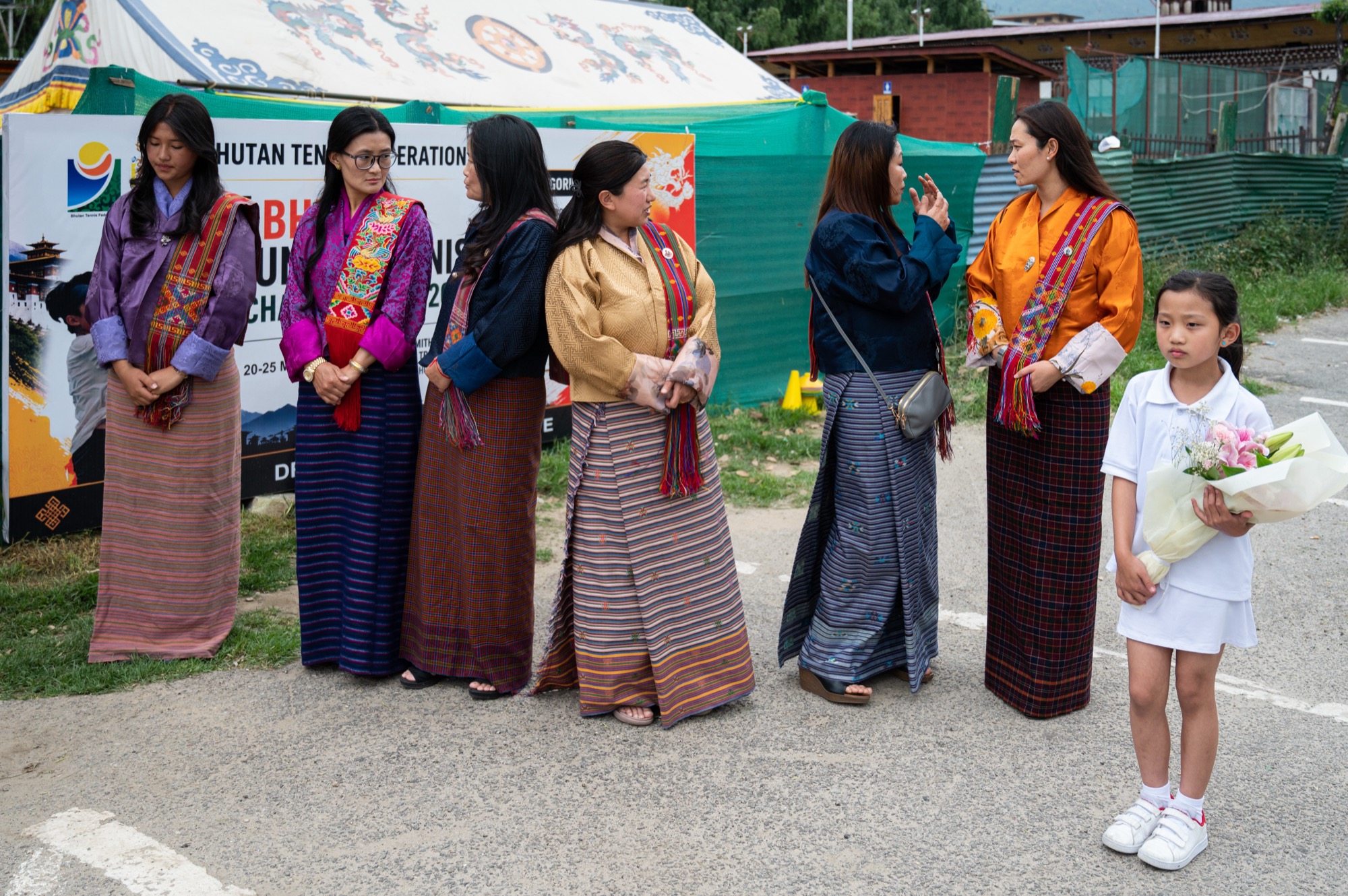 Members and family in Bhutanese national dress courtside, a young player holding a bouquet