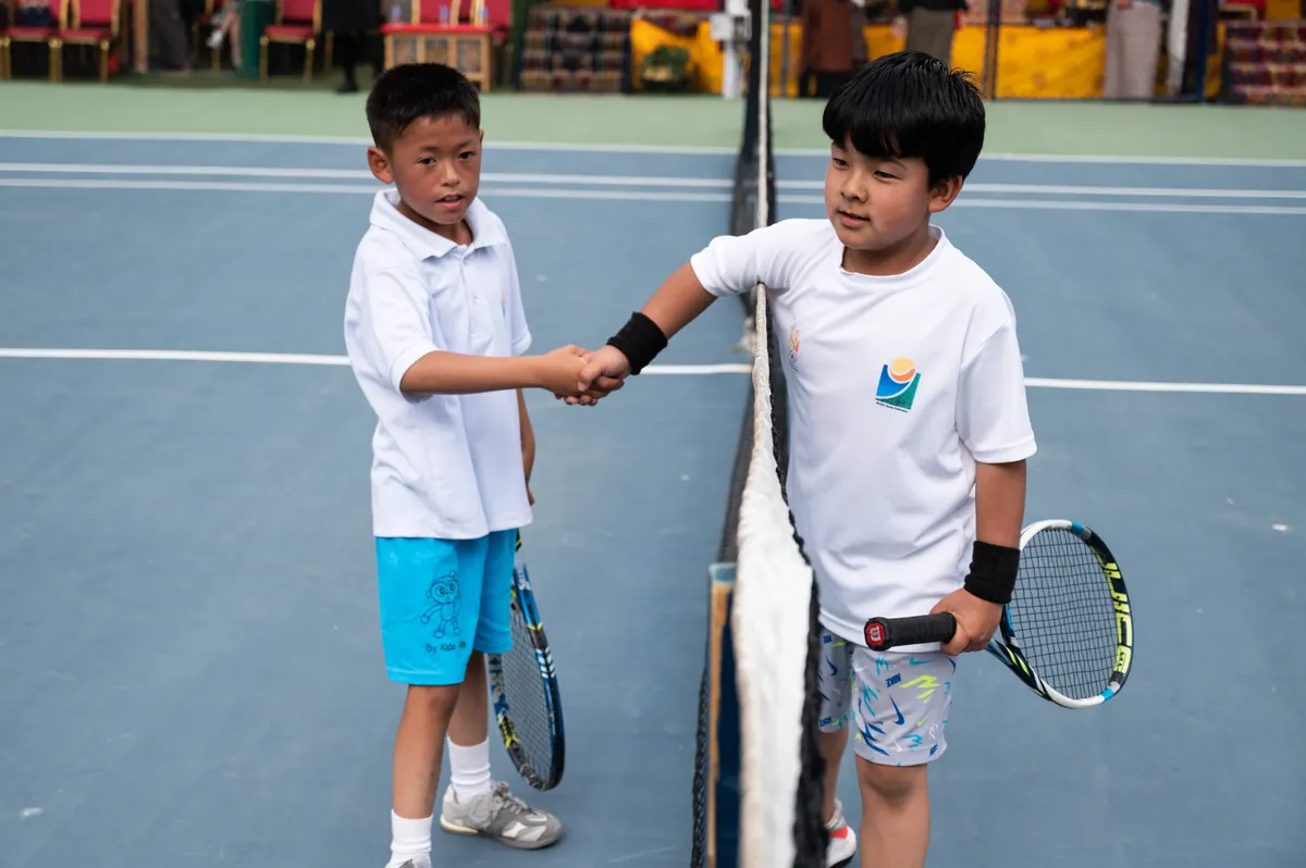 Two junior players shaking hands over the net after their match