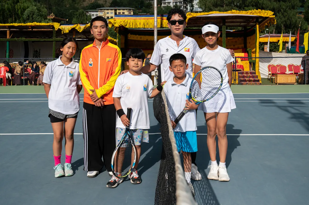 A coach and a group of junior players lined up along the net for a photograph