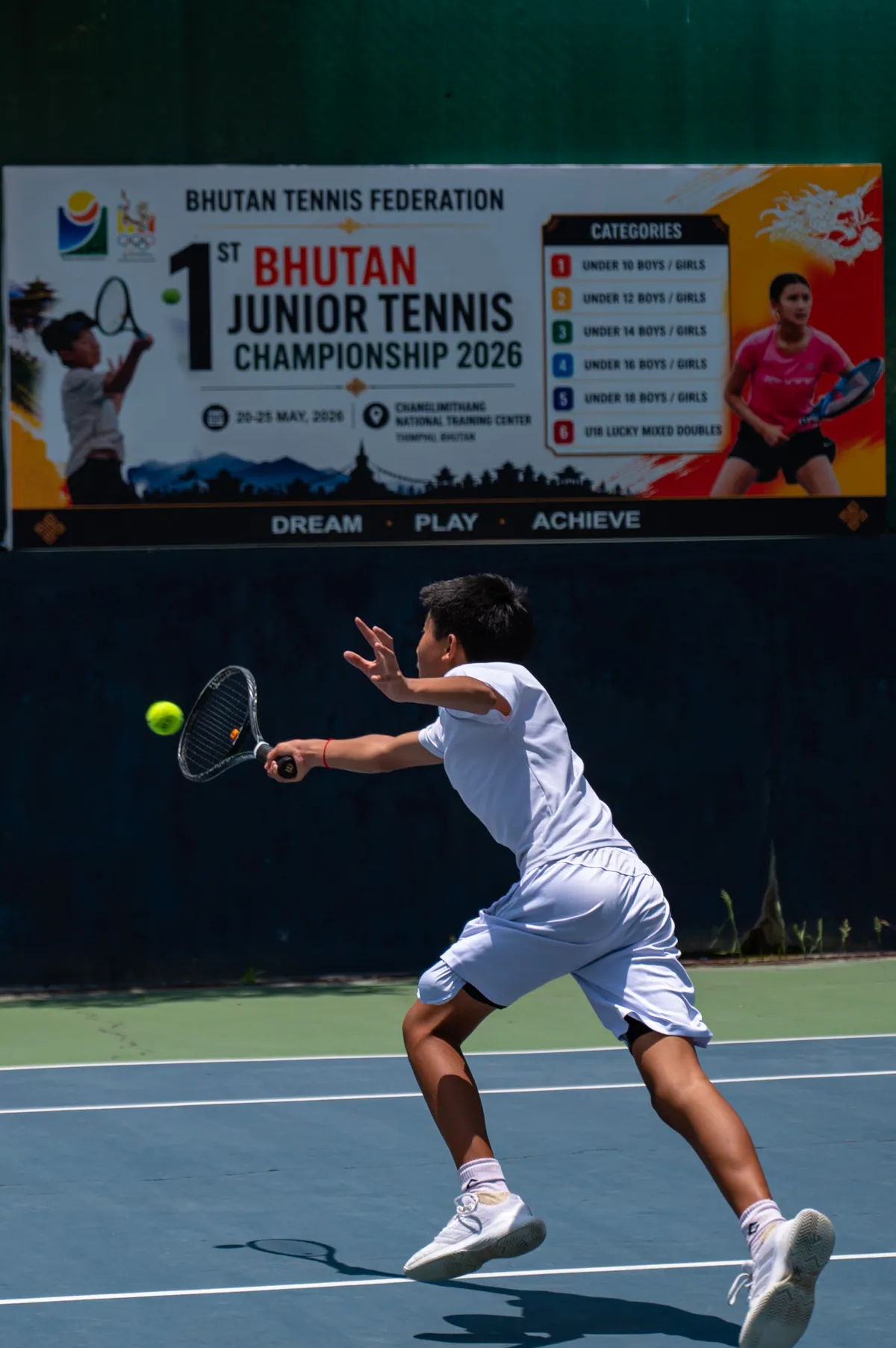 A junior driving a forehand in front of the 1st Bhutan Junior Tennis Championship banner