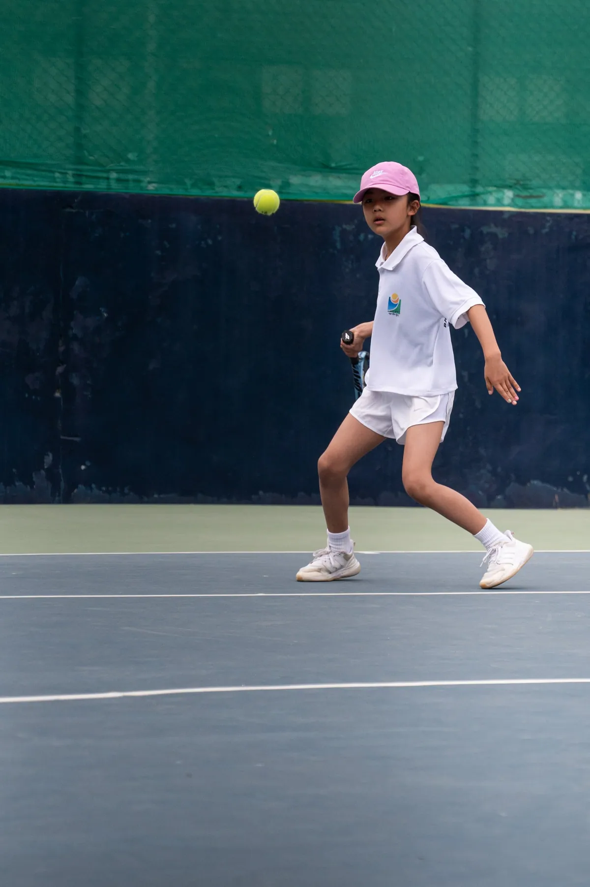 A young player in a pink cap tracking the ball across the baseline