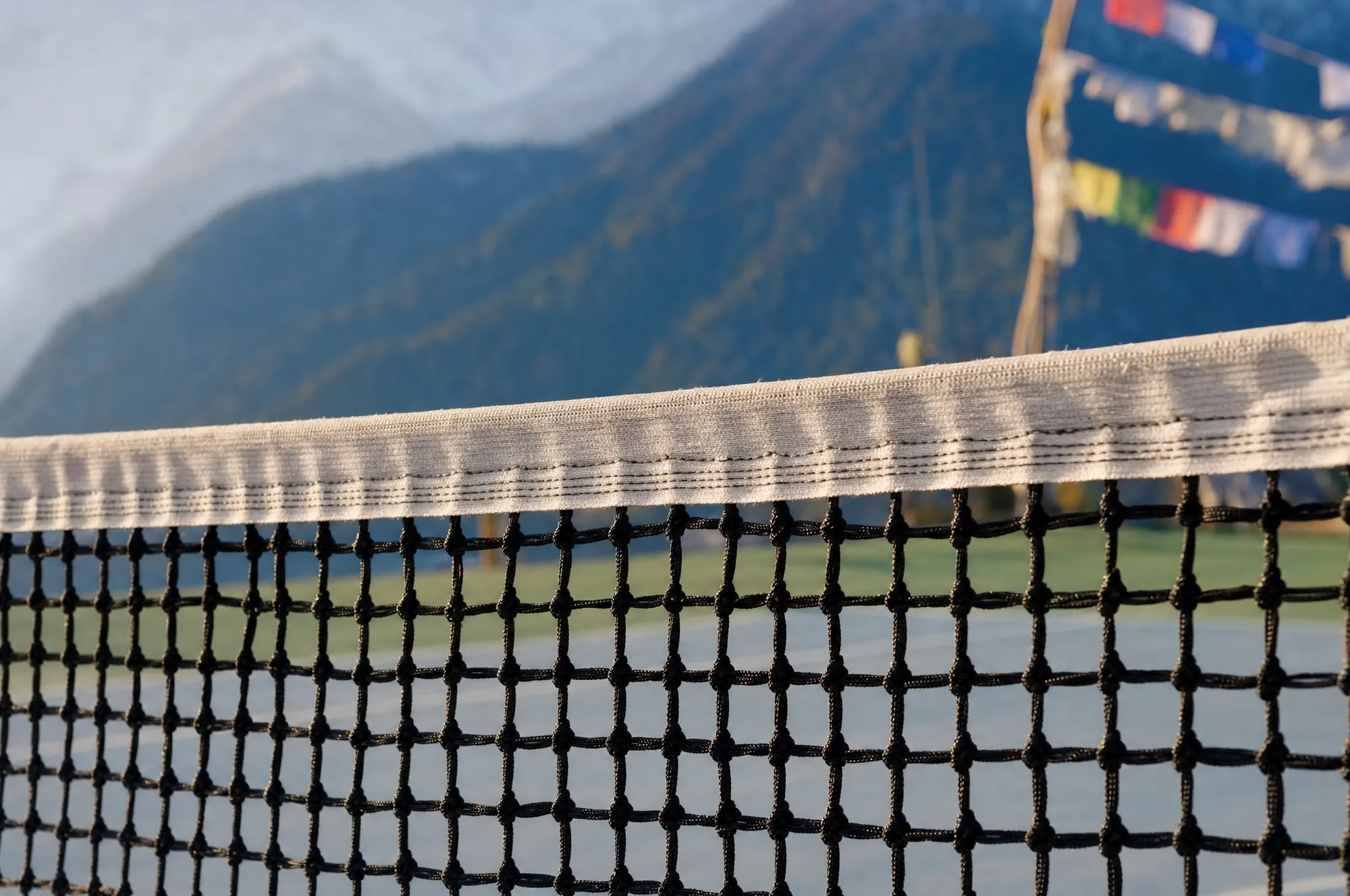 The tape of a tennis net in close-up, prayer flags and the snow-capped Himalaya out of focus beyond
